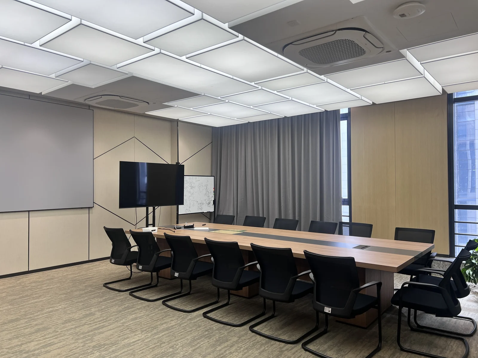 从侧面拍摄的会议长桌与座椅，前方摆放显示屏和白板